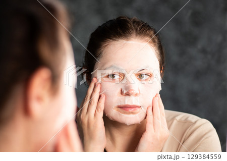 Female applying moisturizing face mask in bathroom. Beauty routine. International Self Care Day. 129384559