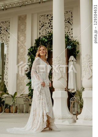 Beautiful slim blonde poses in boho wedding dresses and an embroidered corset on a summer terrace Beautiful slim blonde poses in boho wedding dresses and an embroidered corset on a summer terrace 129384631