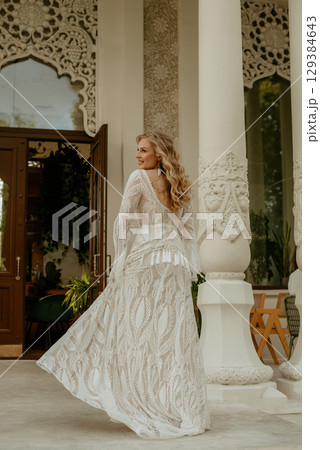 Beautiful slim blonde poses in boho wedding dresses and an embroidered corset on a summer terrace Beautiful slim blonde poses in boho wedding dresses and an embroidered corset on a summer terrace 129384643