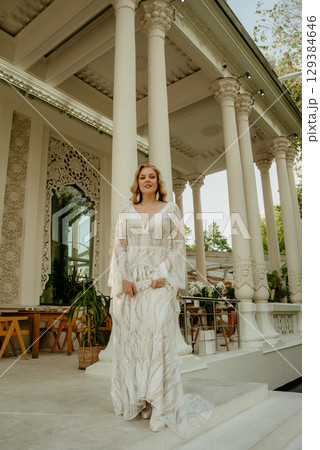 Beautiful slim blonde poses in boho wedding dresses and an embroidered corset on a summer terrace Beautiful slim blonde poses in boho wedding dresses and an embroidered corset on a summer terrace 129384646