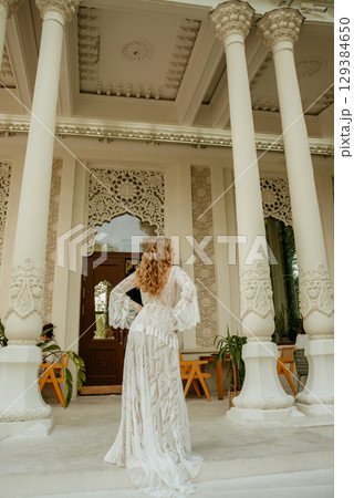 Beautiful slim blonde poses in boho wedding dresses and an embroidered corset on a summer terrace Beautiful slim blonde poses in boho wedding dresses and an embroidered corset on a summer terrace 129384650