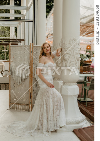 Beautiful slim blonde poses in boho wedding dresses and an embroidered corset on a summer terrace 129384669