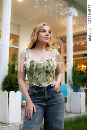 Beautiful slim blonde poses in boho wedding dresses and an embroidered corset on a summer terrace 129384677
