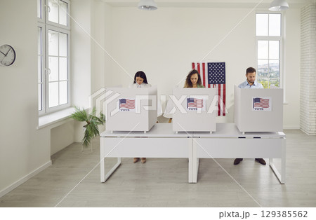 American citizens standing at vote center in voting booth at polling station on election day. 129385562