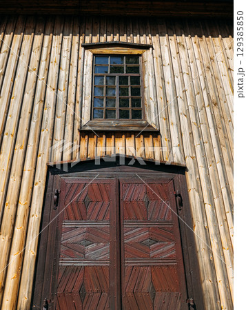 Entrance of a traditional wooden building with a patterned dark wood door and a gridded window above. Architectural heritage, wooden craftsmanship, vernacular design, historical preservation 129385850