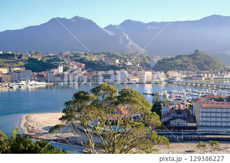A beautiful panoramic view of a coastal town nestled between a tranquil body of water and majestic mountains under a clear blue sky. Ribadesella, Asturias A beautiful panoramic view of a coastal town nestled between a tranquil body of water and majestic mountains under a clear blue sky. Ribadesella, Asturias 129386227