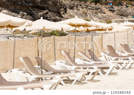 海岸沿いの広々とした砂浜に並べられたパラソルとビーチベッド　フエルテベンテュラ島にて 129386548