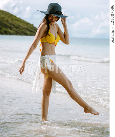 woman in  yellow bikini is walking in the water 129387096