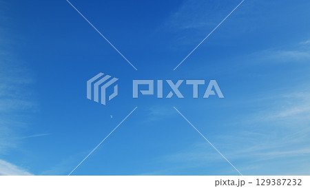 A Serene, Expansive Blue Sky adorned with Wispy Clouds and a Bright, Glowing Moon hanging overhead 129387232