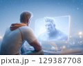 Man looks at mesmerizing holographic character on large screen, showcasing advanced technology in a cozy room. Soft lighting captures a tranquil evening atmosphere. 129387708