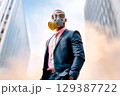 Businessman stands confidently in a suit and gas mask, symbolizing strength in challenging environments. Urban backdrop filled with smoke creates a dramatic atmosphere. 129387722