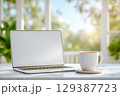 Laptop sits on kitchen counter next to coffee mug, warm morning sunlight streaming through window. Bright atmosphere creates inviting setting for home workspace. 129387723