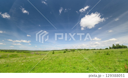 A Vibrant Green Field Lushly Spreads Under a Bright Blue Sky with Beautiful Fluffy Clouds 129388051