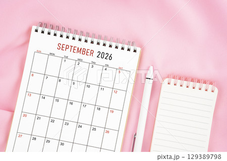 September 2026 month calendar and pen with open diary on pink color fabric background. 129389798
