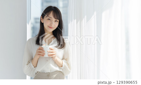 窓際に立ってマグカップを持つ女性 129390655