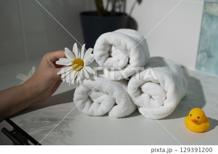 Hand Holding a Flower Near Rolled Towels and a Rubber Duck on a Marble Countertop Hand Holding a Flower Near Rolled Towels and a Rubber Duck on a Marble Countertop 129391200