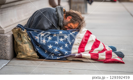 Homeless man sleeping on the sidewalk in the USA, hiding behind an American flag Homeless man sleeping on the sidewalk in the USA, hiding behind an American flag 129392459