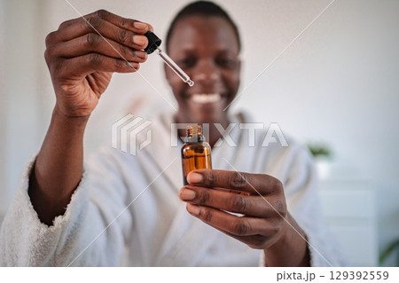 Smiling young man using essential oils for skin care Smiling young man using essential oils for skin care 129392559