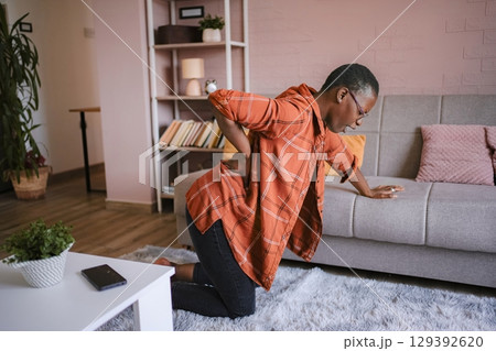 Young woman suffering back pain at home, kneeling on the floor Young woman suffering back pain at home, kneeling on the floor 129392620