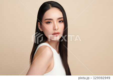 A beautiful young Asian woman with clean, fresh skin against a beige background. Skincare, facial treatment, cosmetology, beauty, and spa. An elegant portrait of an Asian woman. A beautiful young Asian woman with clean, fresh skin against a beige background. Skincare, facial treatment, cosmetology, beauty, and spa. An elegant portrait of an Asian woman. 129392949