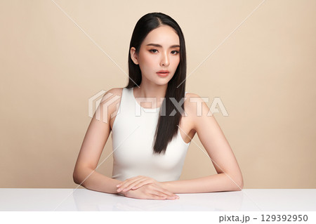 A beautiful young Asian woman with clean, fresh skin against a beige background. Skincare, facial treatment, cosmetology, beauty, and spa. An elegant portrait of an Asian woman. 129392950