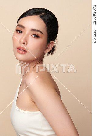 A beautiful young Asian woman with clean, fresh skin against a beige background. Skincare, facial treatment, cosmetology, beauty, and spa. An elegant portrait of an Asian woman. 129392973