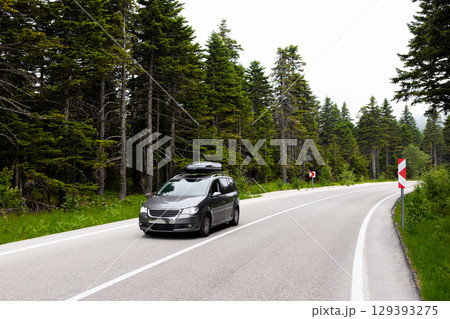 Minivan driving on curved forest road with lush greenery and overcast sky 129393275