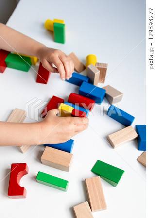Child playing with colorful wooden building blocks on white surface Child playing with colorful wooden building blocks on white surface 129393277