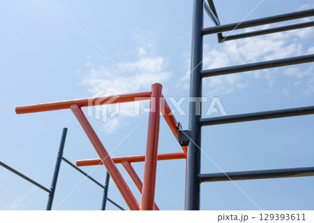 A vibrant orange fitness structure stands against a clear blue sky, inviting outdoor enthusiasts to engage in physical activity under the sun 129393611