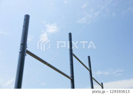 Vertical bars create a workout station for users in a serene park setting under a bright sky with few clouds 129393613
