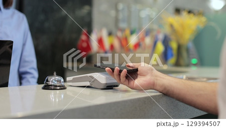 Customer with mobile phone pay for hotel reception, payment. Client, concierge service or people at help desk. Person at reception desk and doing check. Close up. 129394507