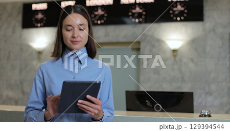Portrait of receptionist woman with tablet in lobby for booking schedule, check in app or reservation. Concierge service, woman smile in lobby for check in assistance, reservation and help. 129394544
