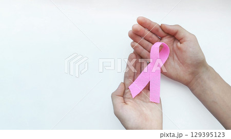 Woman holding pink ribbon as symbol of World Cancer day, breast cancer awareness sign . Campaign to give helping hand to person who facing cancer disease. White background, copy space. Woman holding pink ribbon as symbol of World Cancer day, breast cancer awareness sign . Campaign to give helping hand to person who facing cancer disease. White background, copy space. 129395123