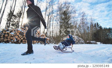 Winter forest scene, father pulling sledding son, sharing playful moments amid snow covered trees and bright sunshine Winter forest scene, father pulling sledding son, sharing playful moments amid snow covered trees and bright sunshine 129395149