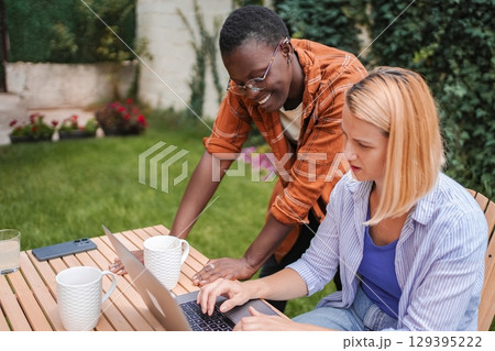 Two female colleagues working on a laptop in the garden 129395222