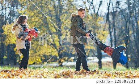 Happy family enjoying a sunny autumn day in a park, playing with their children among colorful fallen leaves Happy family enjoying a sunny autumn day in a park, playing with their children among colorful fallen leaves 129395231