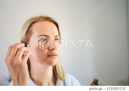 Woman applying essential oil on her face for skin care treatment 129395232