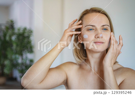 Woman applying face cream at home 129395246