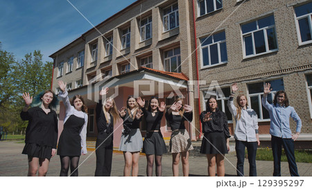 Joyful group of students waving in front of a school building on a sunny summer day, celebrating togetherness and success Joyful group of students waving in front of a school building on a sunny summer day, celebrating togetherness and success 129395297