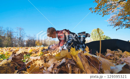 Mother and son enjoying playful moments in a park, lying together on vibrant autumn leaves under a warm, sunny sky Mother and son enjoying playful moments in a park, lying together on vibrant autumn leaves under a warm, sunny sky 129395321