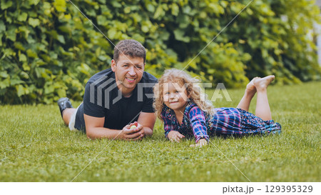 Father with daughter resting on green lawn, sharing intimate moment during outdoor bonding time 129395329