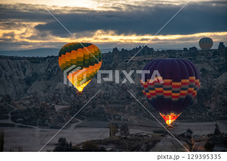 Colorful hot air balloons glowing in early morning dawn flying over mountain landscape 129395335