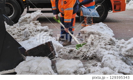 Tractor shovel loading snow and ice into truck during winter road cleaning 129395343