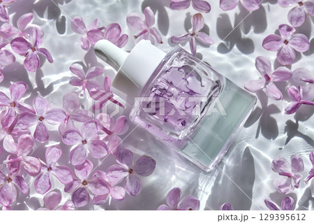 A bottle of hyaluronic serum in lilac flowers in the water. 129395612