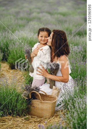 Mother with little daughter on lavender background. Beautiful woman and cute baby playing in meadow field. Family holiday in summer day. 129396998