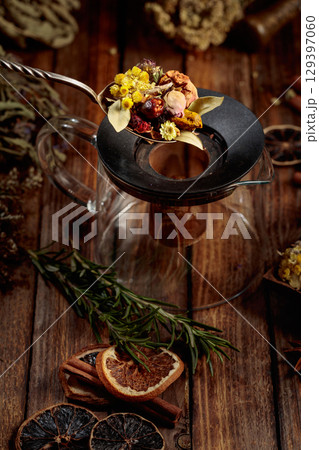 Various dried herbs and spices is poured into a glass teapot. Various dried herbs and spices is poured into a glass teapot. 129397060