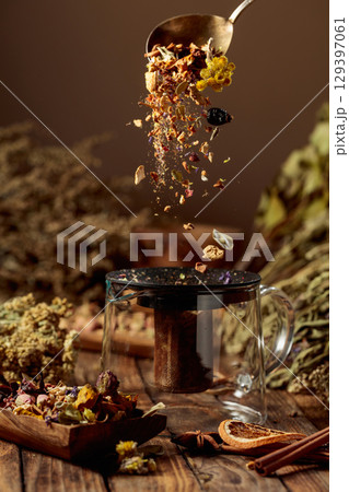 Various dried herbs and spices is poured into a glass teapot. 129397061