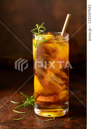 Iced tea or cocktail with ice, rosemary and lemon slices on the old brown table. Iced tea or cocktail with ice, rosemary and lemon slices on the old brown table. 129397081