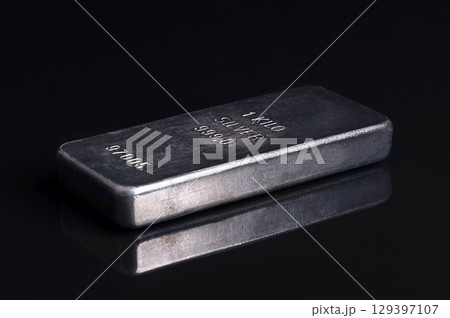 Old and scratched silver bar, side view, on black glass. Stamped and numbered cast silver ingot, of one kilogram, about 32 troy oz of metal, with a purity of 999.0, that is 99.9 percent pure silver. 129397107
