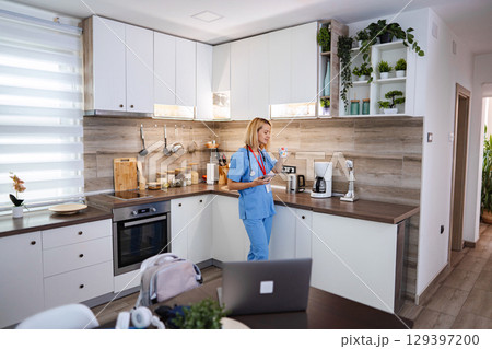 Female Doctor Drinking Tea and Using Smartphone in Kitchen during Work Break 129397200